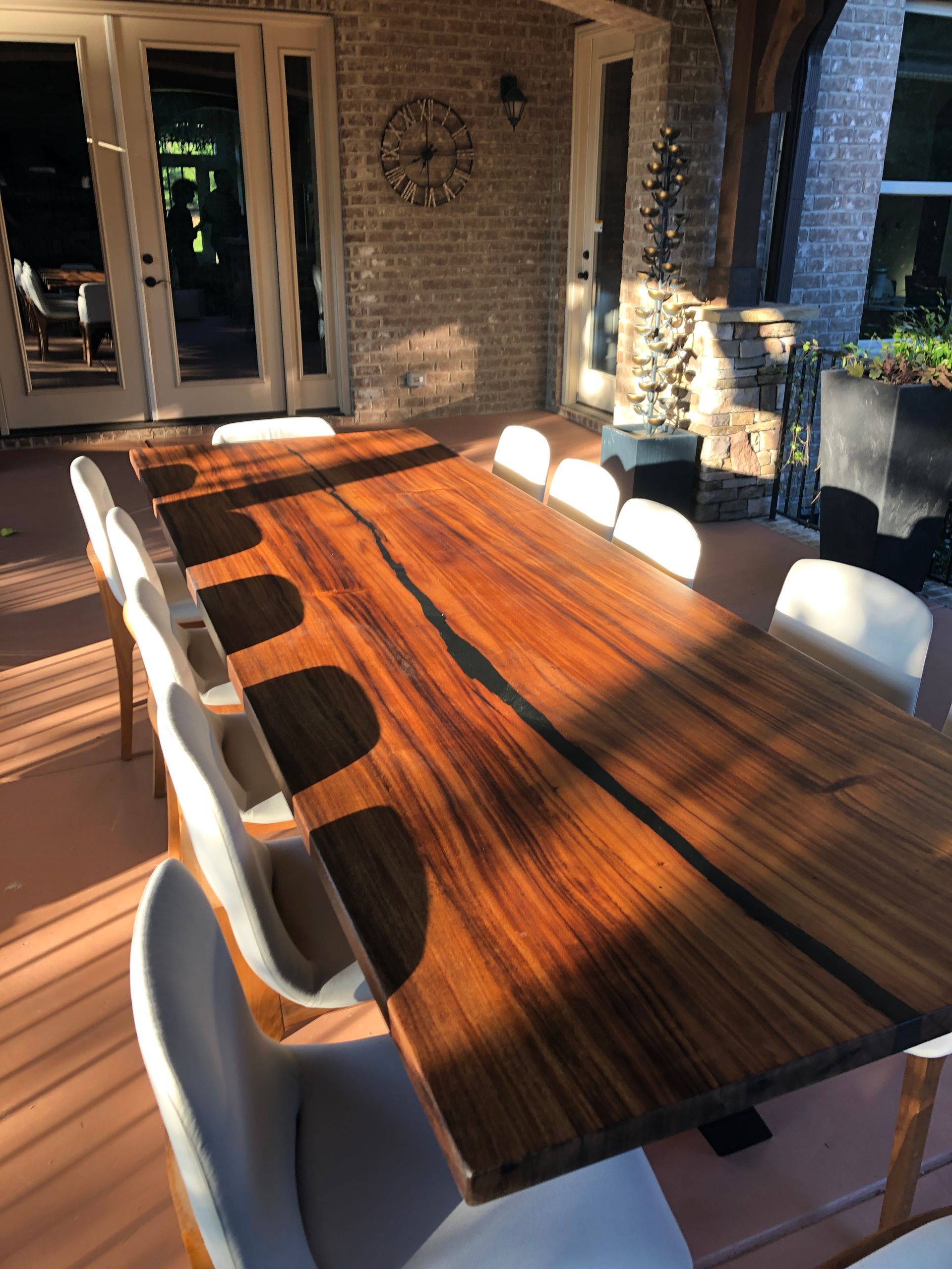 Outdoor dining table with ten white chairs, on a brick patio.