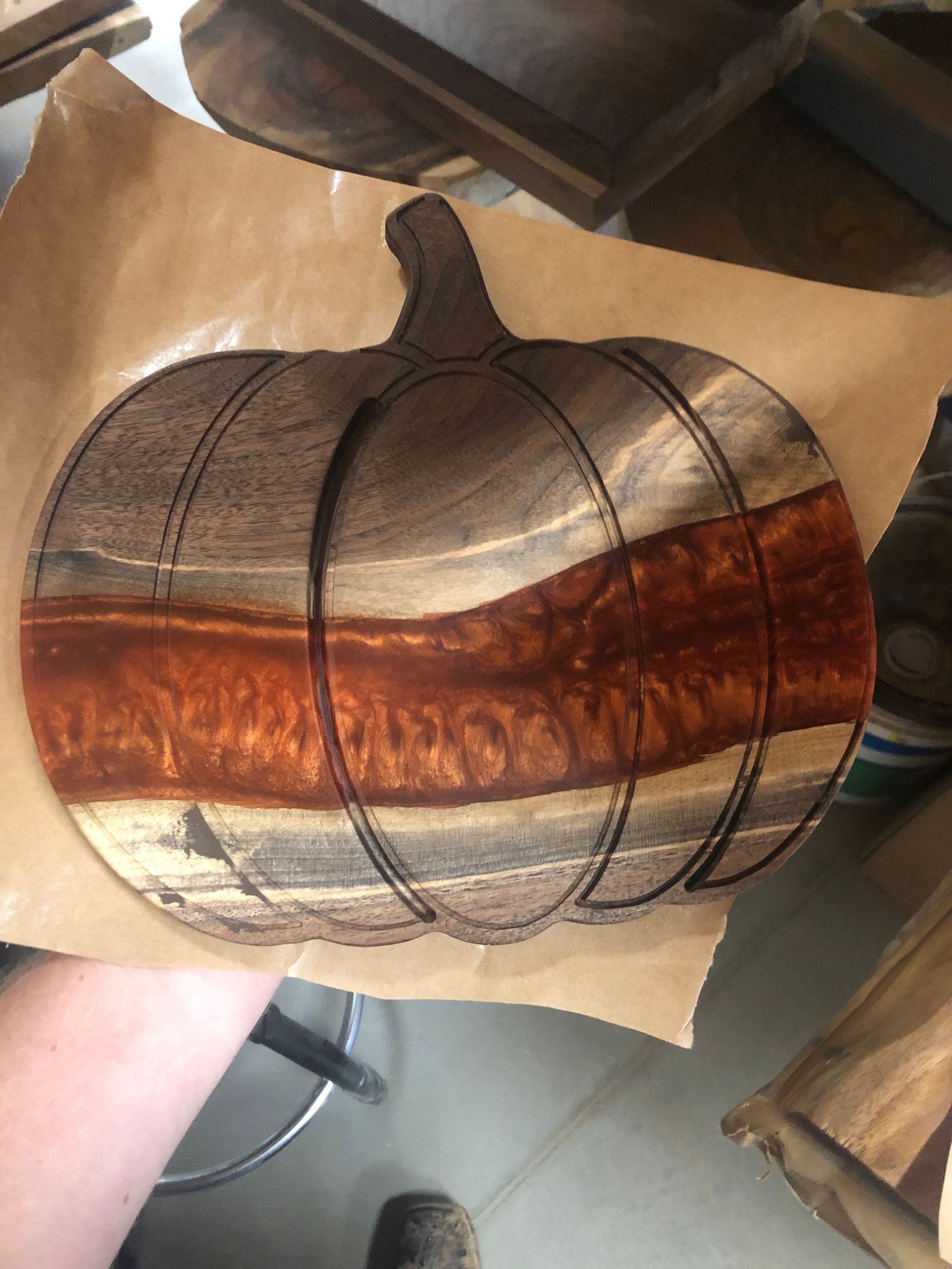 A person is holding a wooden pumpkin on a piece of paper.