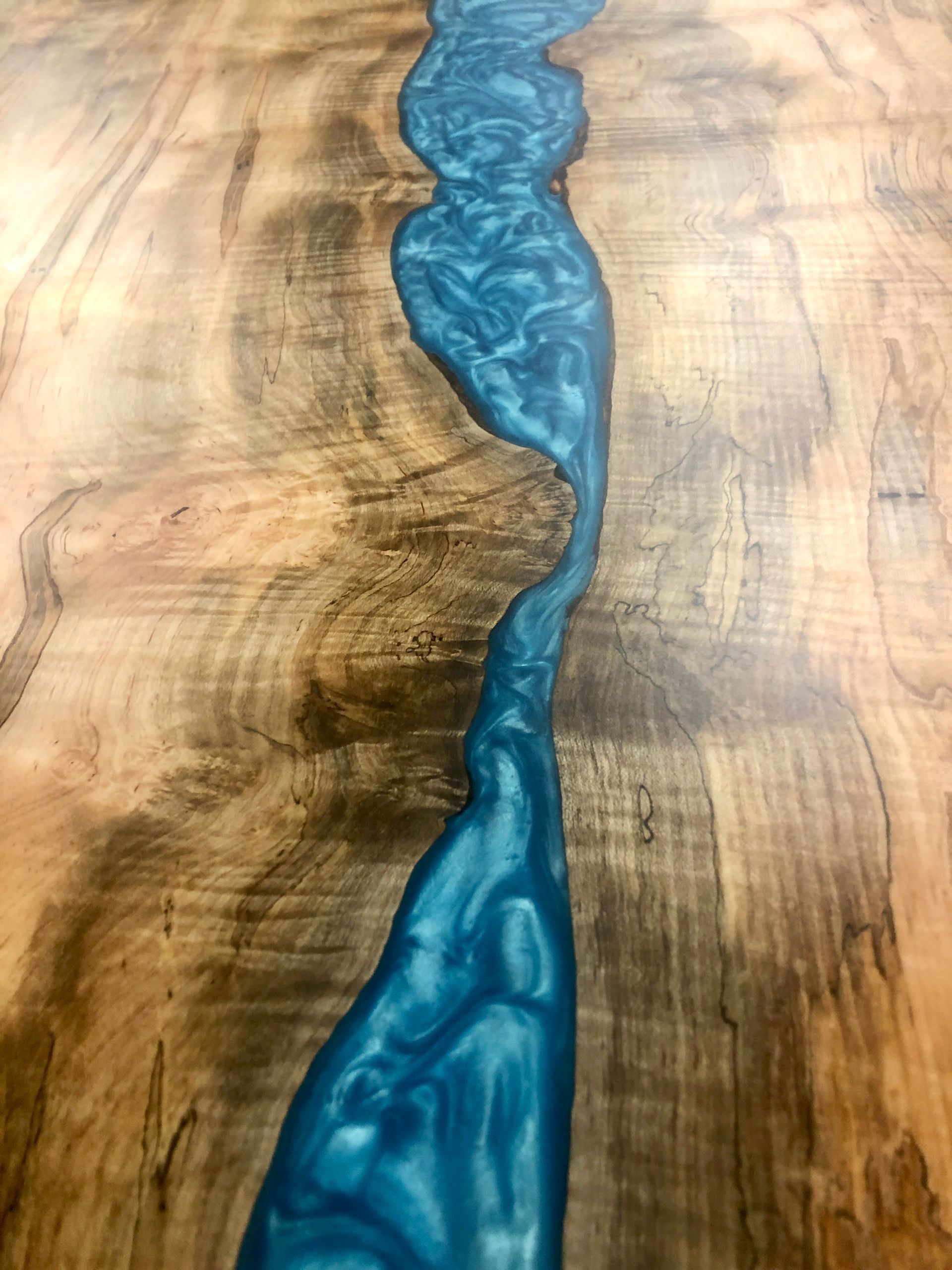 A Maple live edge wooden table with a blue  epoxy river joining the table. 