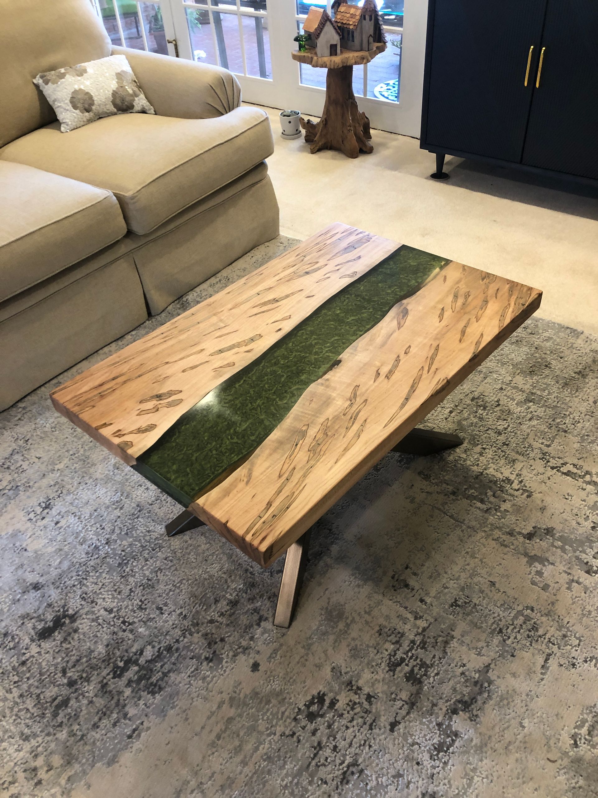 Wooden coffee table with green resin river inlay, in a living room.