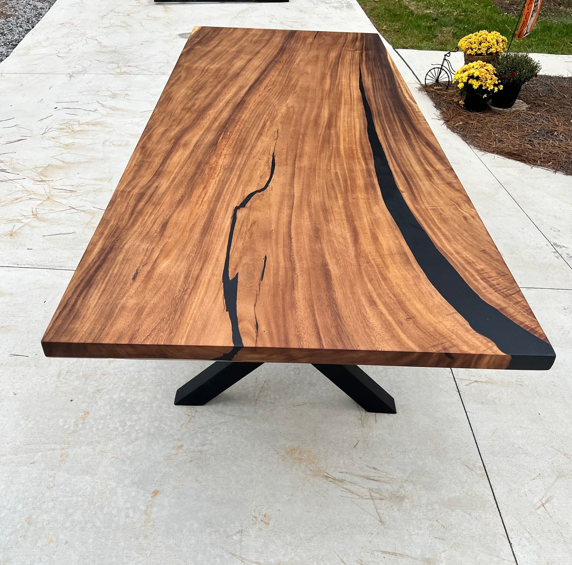 Wooden table with black resin river, on a black metal base, outdoors.