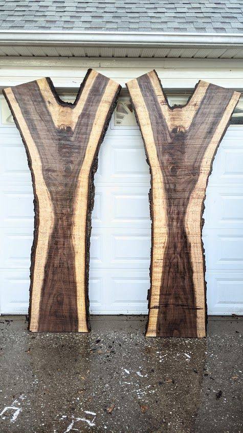 Two vertically-oriented walnut wood slabs with a light-colored edge and dark center grain, leaning against a garage door.