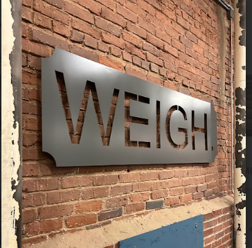 A sign on a brick wall that says weigh