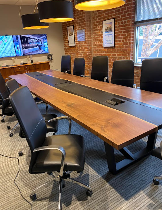 Conference room with large wooden table, black chairs, brick wall, and hanging lights.