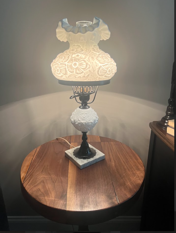 Bedside table with cup and saucer beside a bed with a dark wood headboard, white bedding.