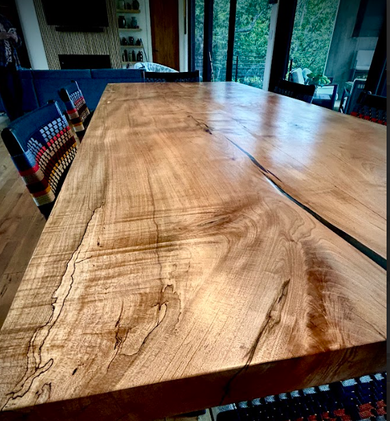 Large live-edge wooden dining table in a modern dining room with chairs and glass doors.