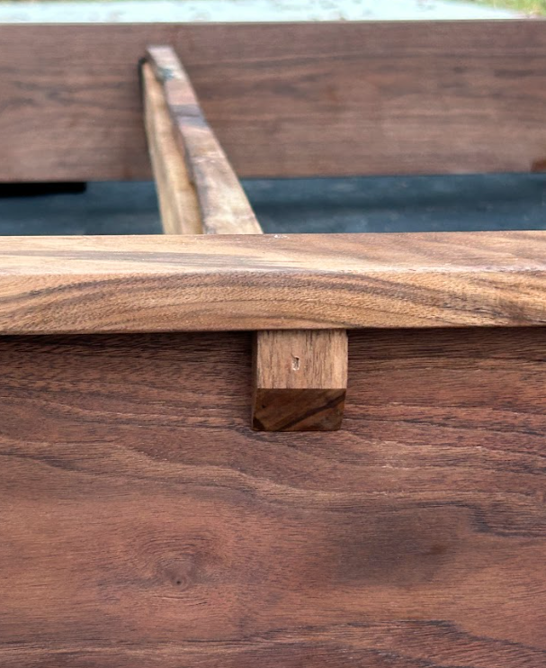 Wooden bed frame detail showing a support beam connected to a side rail. Brown wood.