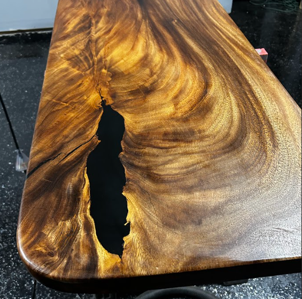 Wooden table with black resin inlay, featuring swirling patterns and a glossy finish.
