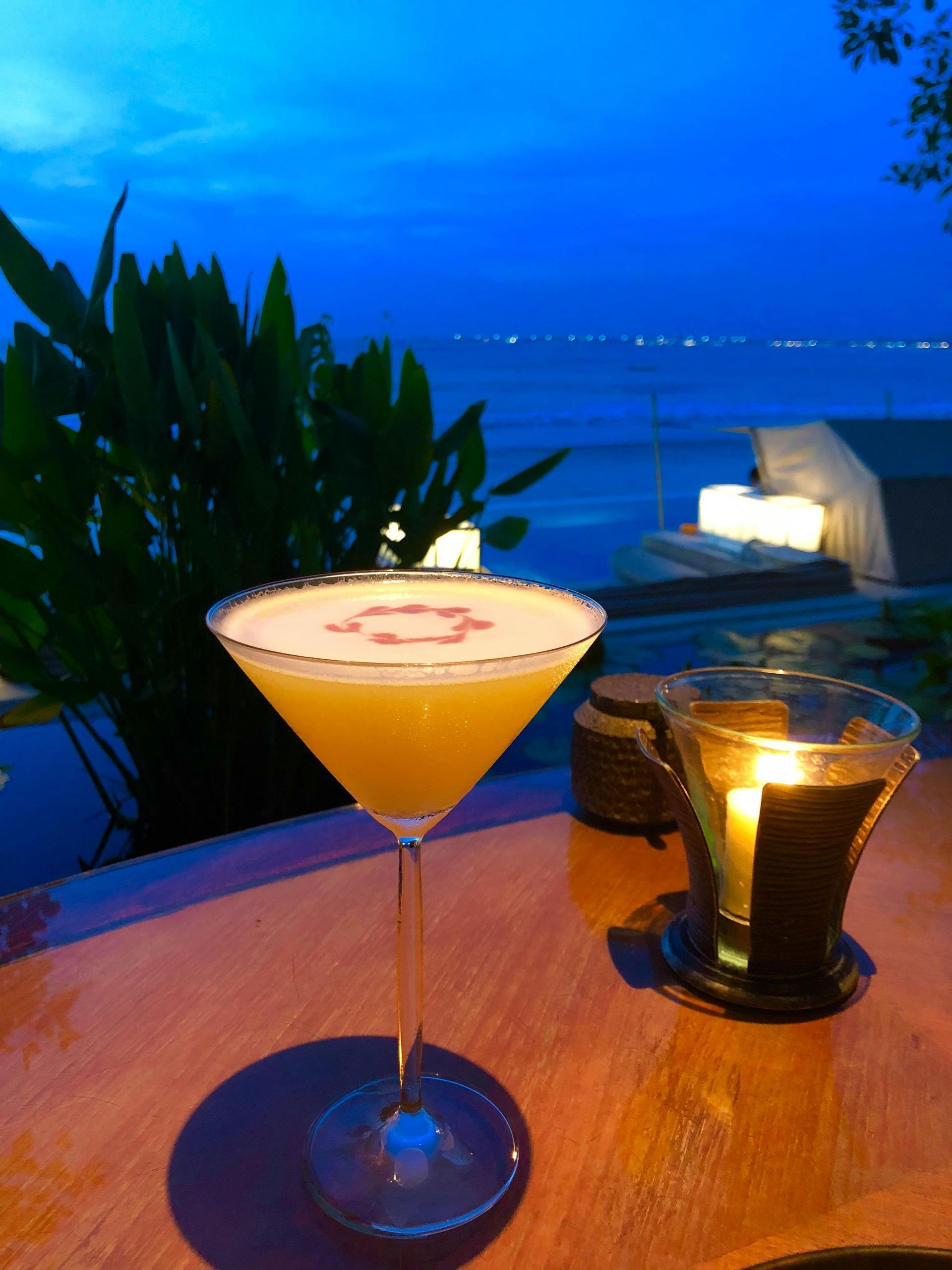 Cocktail on a table, sunset over the ocean in the background. Candlelit ambiance.