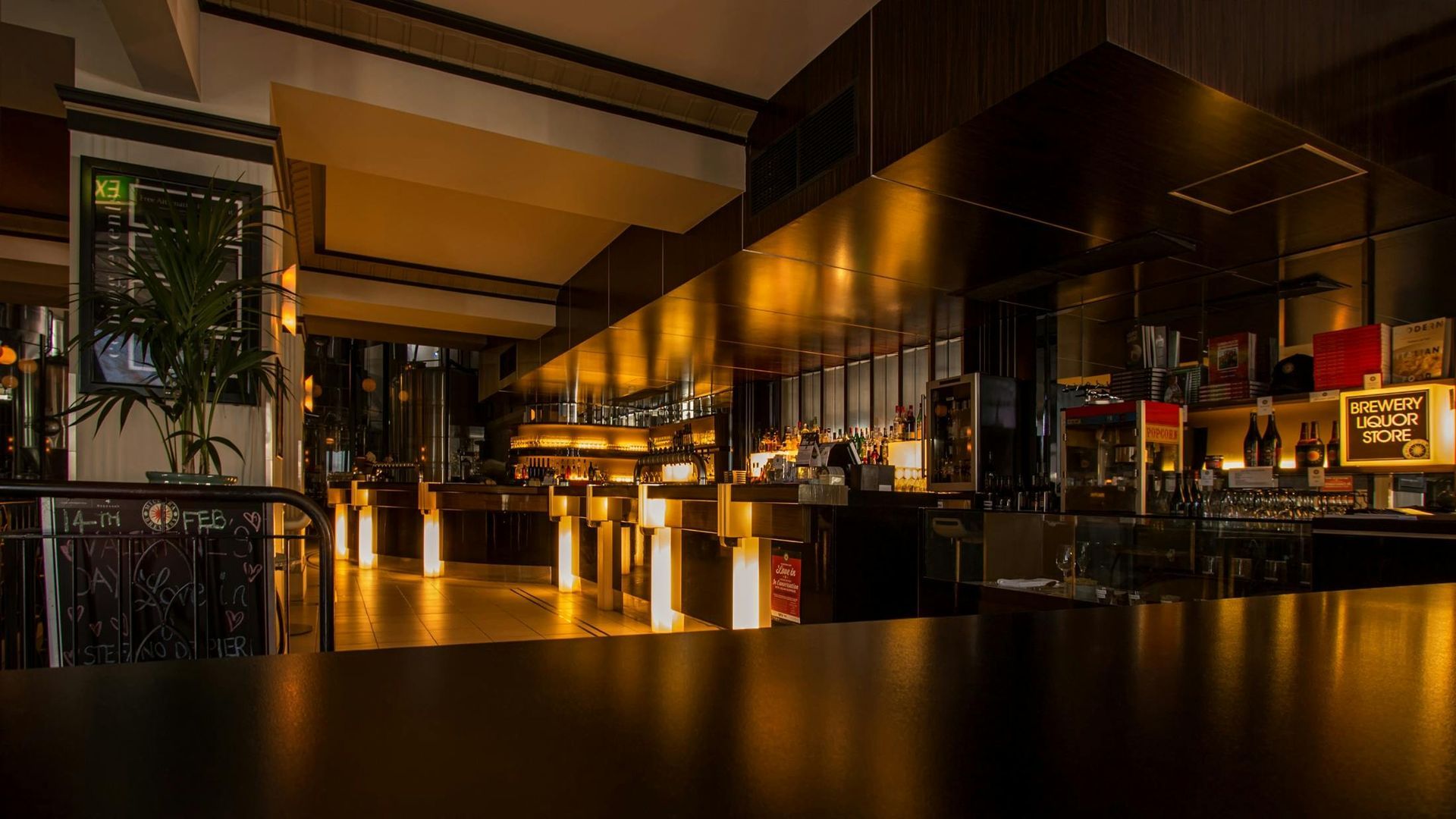 Dark, well-lit bar interior. Long bar with stools, wooden paneling, and bottles behind the bar.