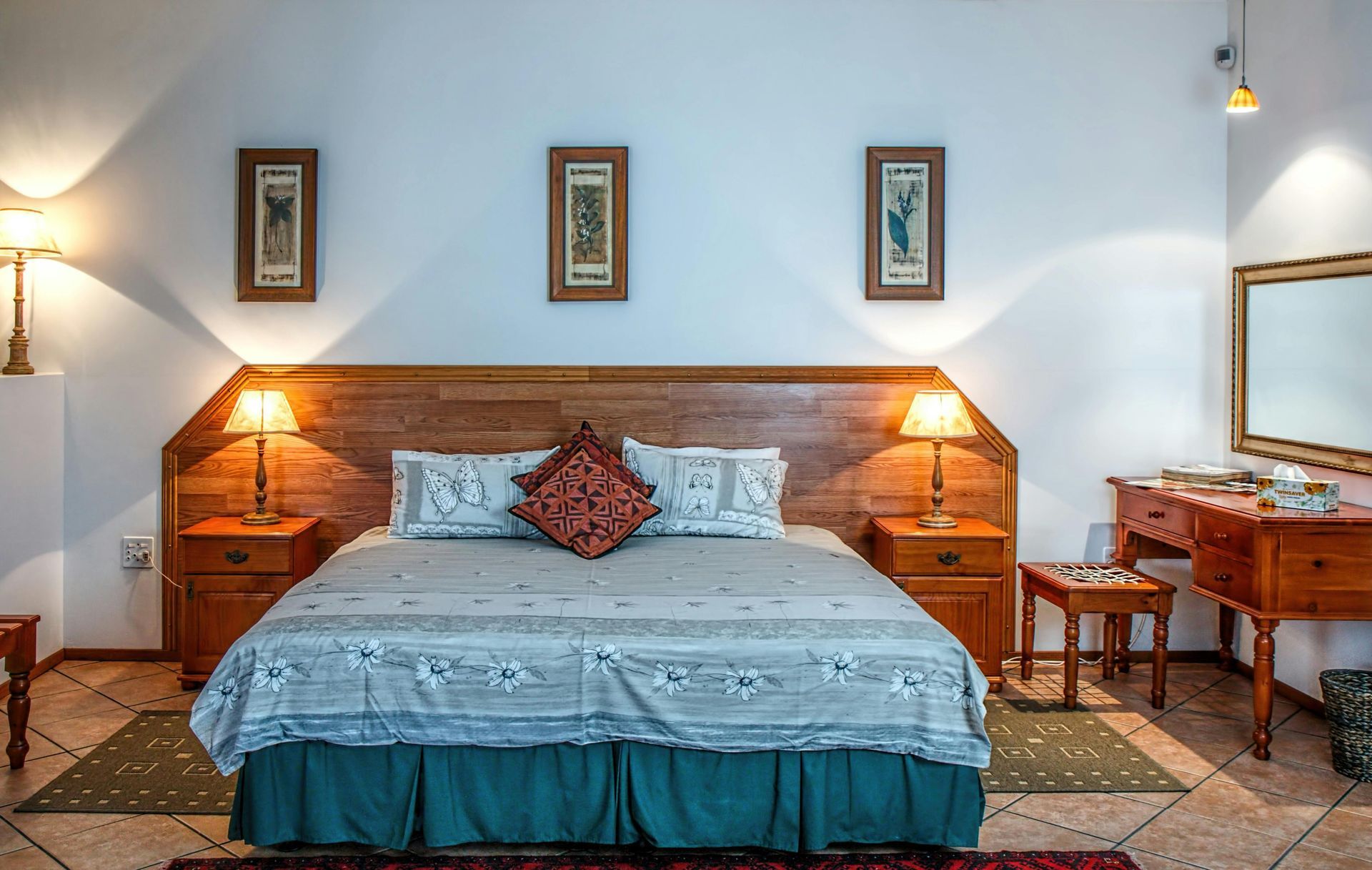 Bedroom with a large wooden headboard, bedside tables with lamps, and a vanity with a mirror.