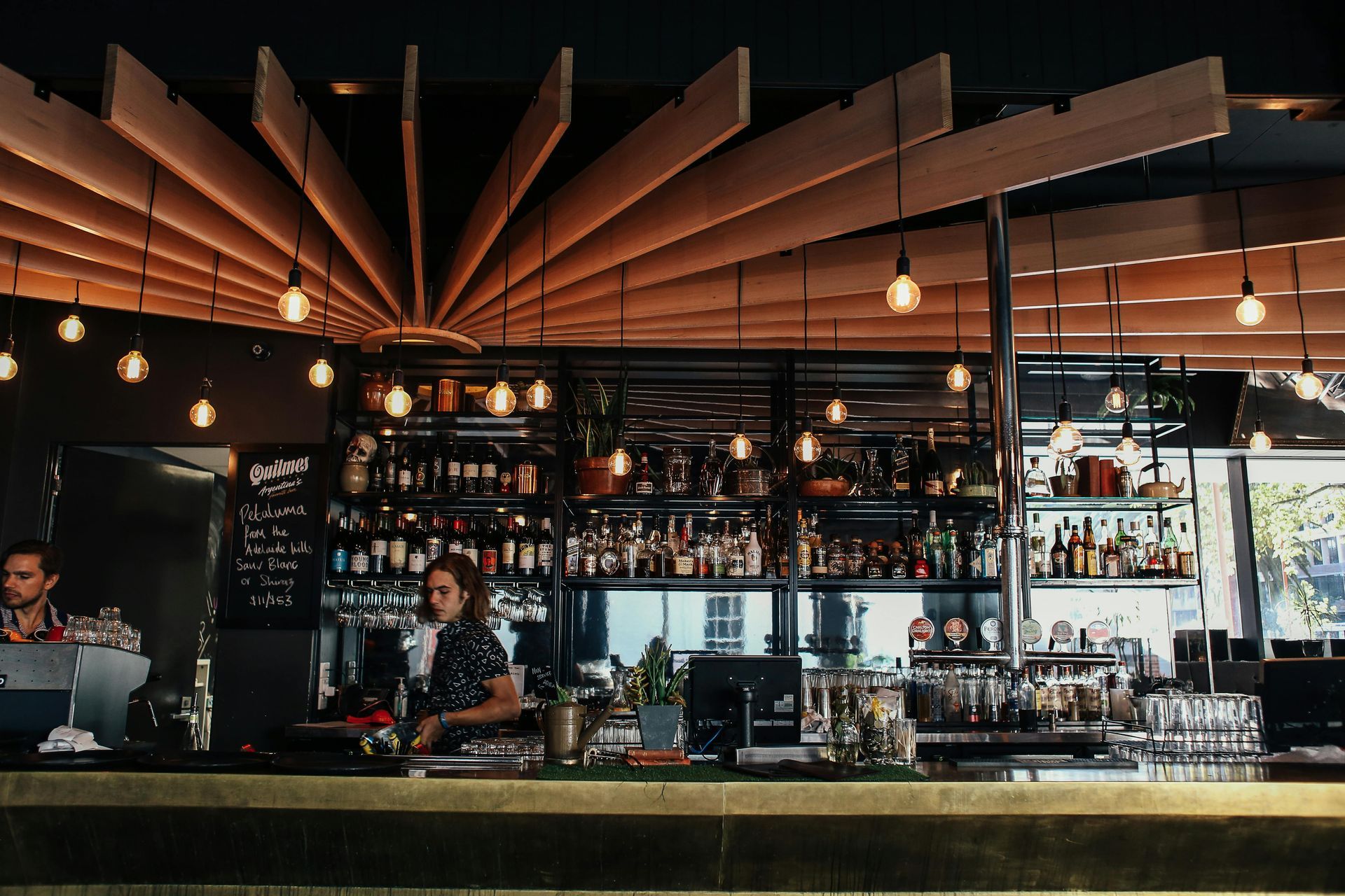 A bar with a wooden ceiling and two bartenders behind it.