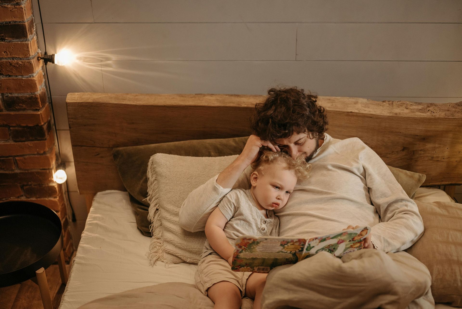 Father reading a book to a child in bed, both relaxed and content.