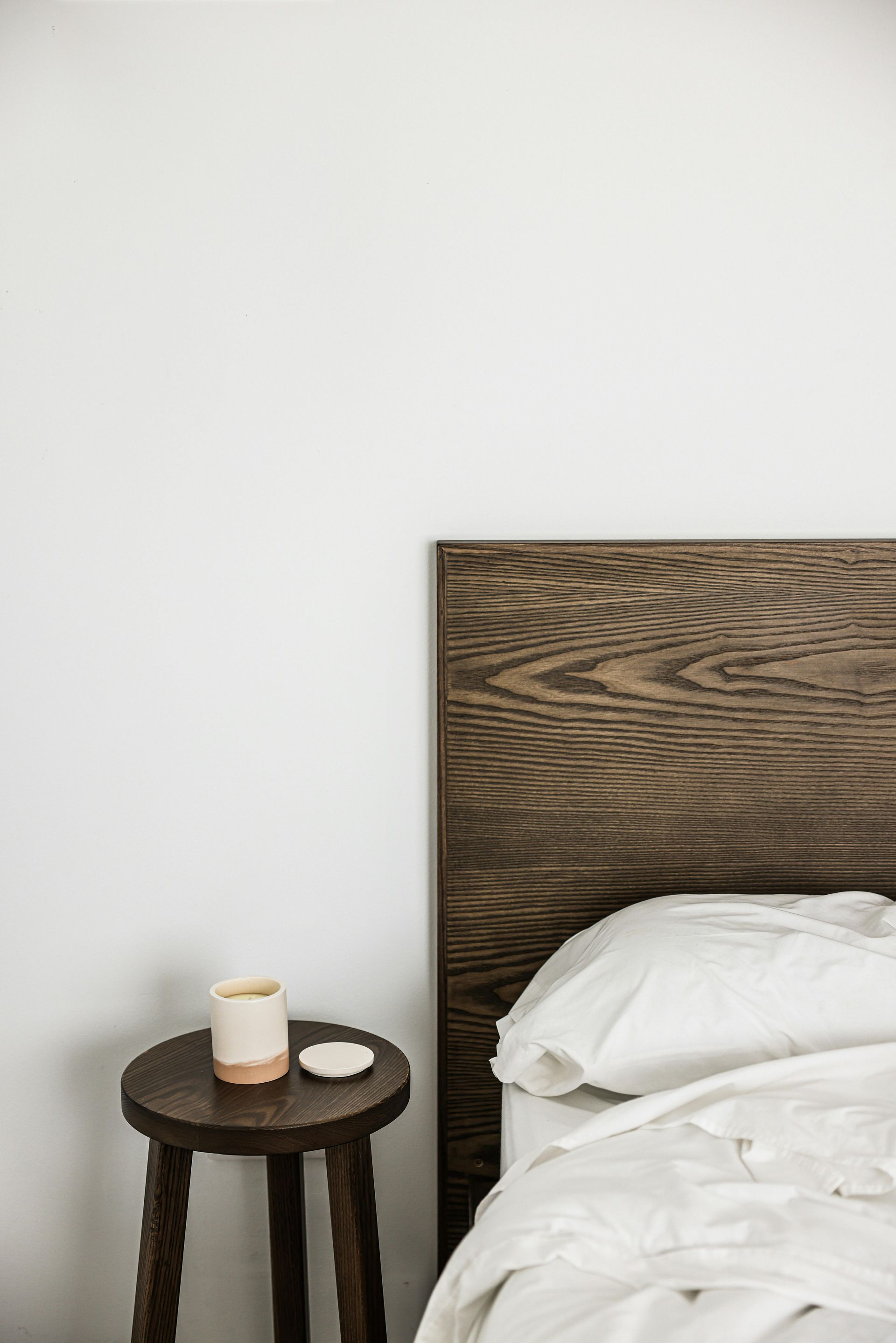 Bedside table with cup and saucer beside a bed with a dark wood headboard, white bedding.