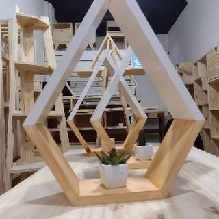 Estantes de madera en forma de diamante con un acabado en madera blanca y natural, que sostienen pequeñas plantas en macetas, sobre un fondo de taller.