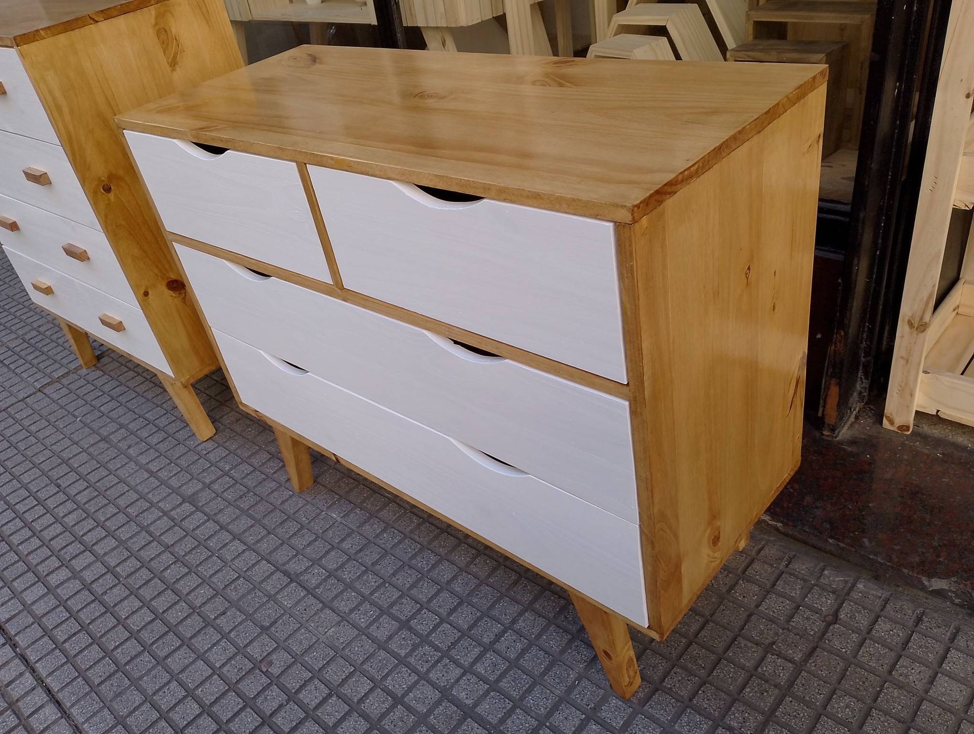Cómoda de madera con cajones blancos, parte superior y laterales de color marrón claro, sobre un patio de ladrillo.