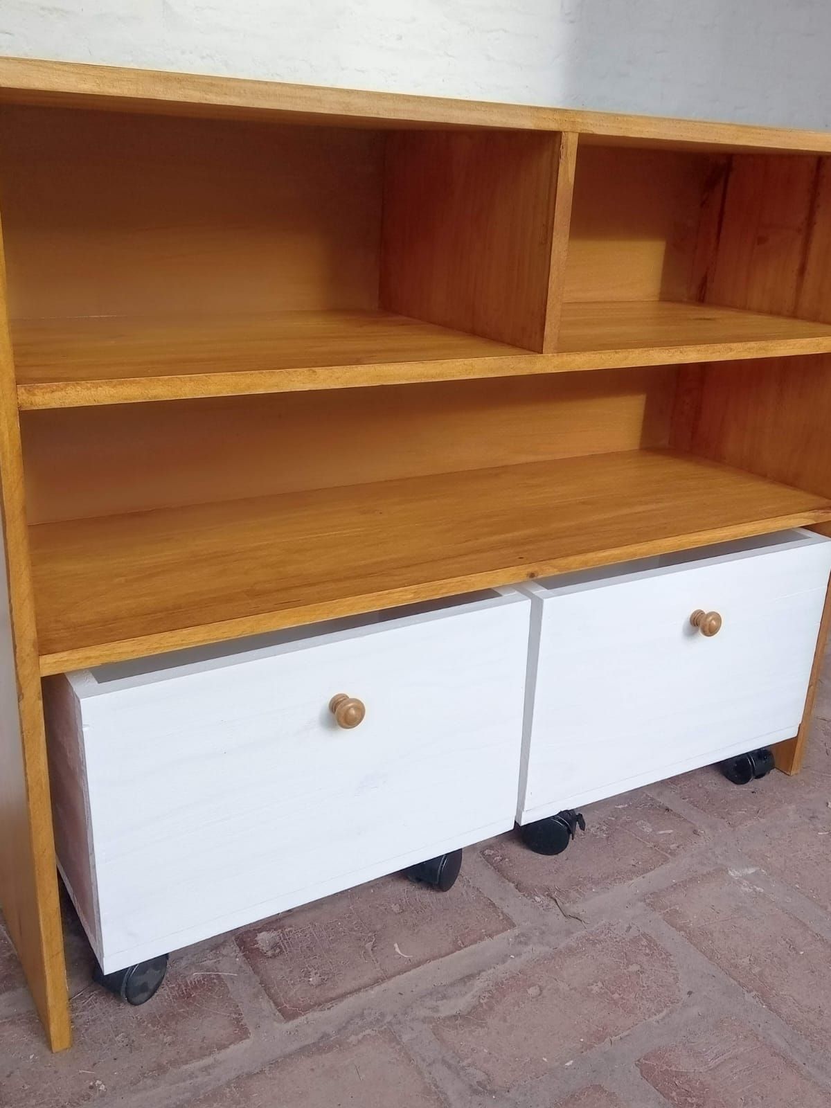 Estantería de madera con dos estantes abiertos, dos cajones blancos y ruedas.