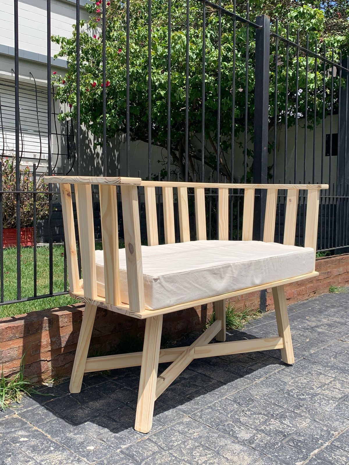 Banco de madera con cojín gris contra un seto verde.