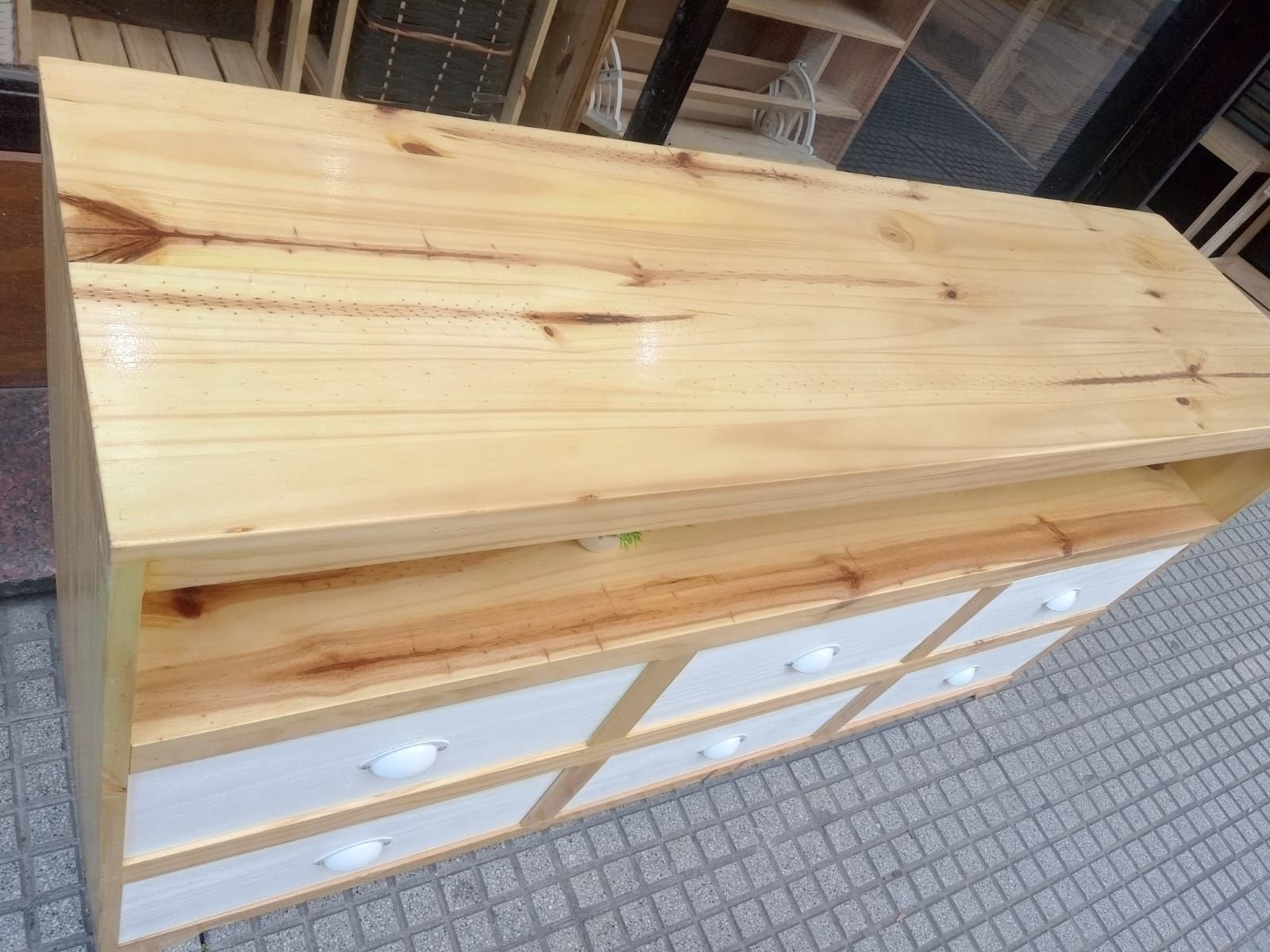 Mueble de TV de madera con seis cajones blancos y estantes abiertos, expuesto en el exterior de una tienda.