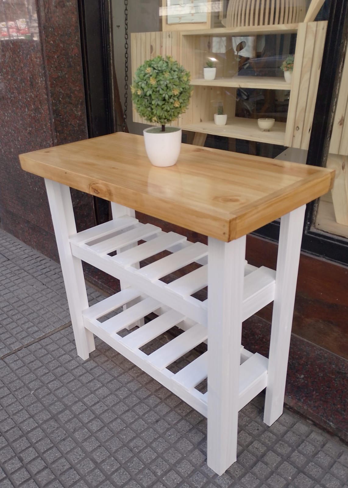 Isla de cocina de madera con encimera de color claro, estructura blanca y dos estantes de listones. Una planta sobre la encimera.
