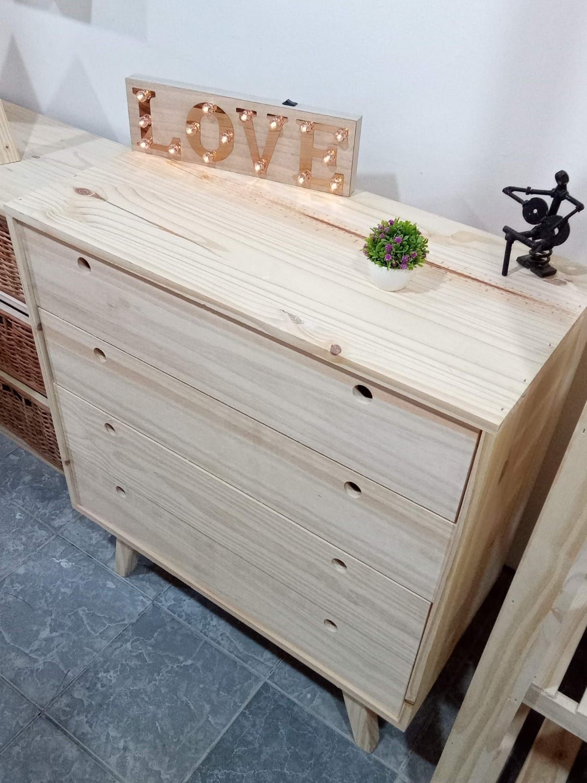 Cómoda de madera de cuatro cajones con pequeños tiradores negros, patas en ángulo y elementos en la parte superior.