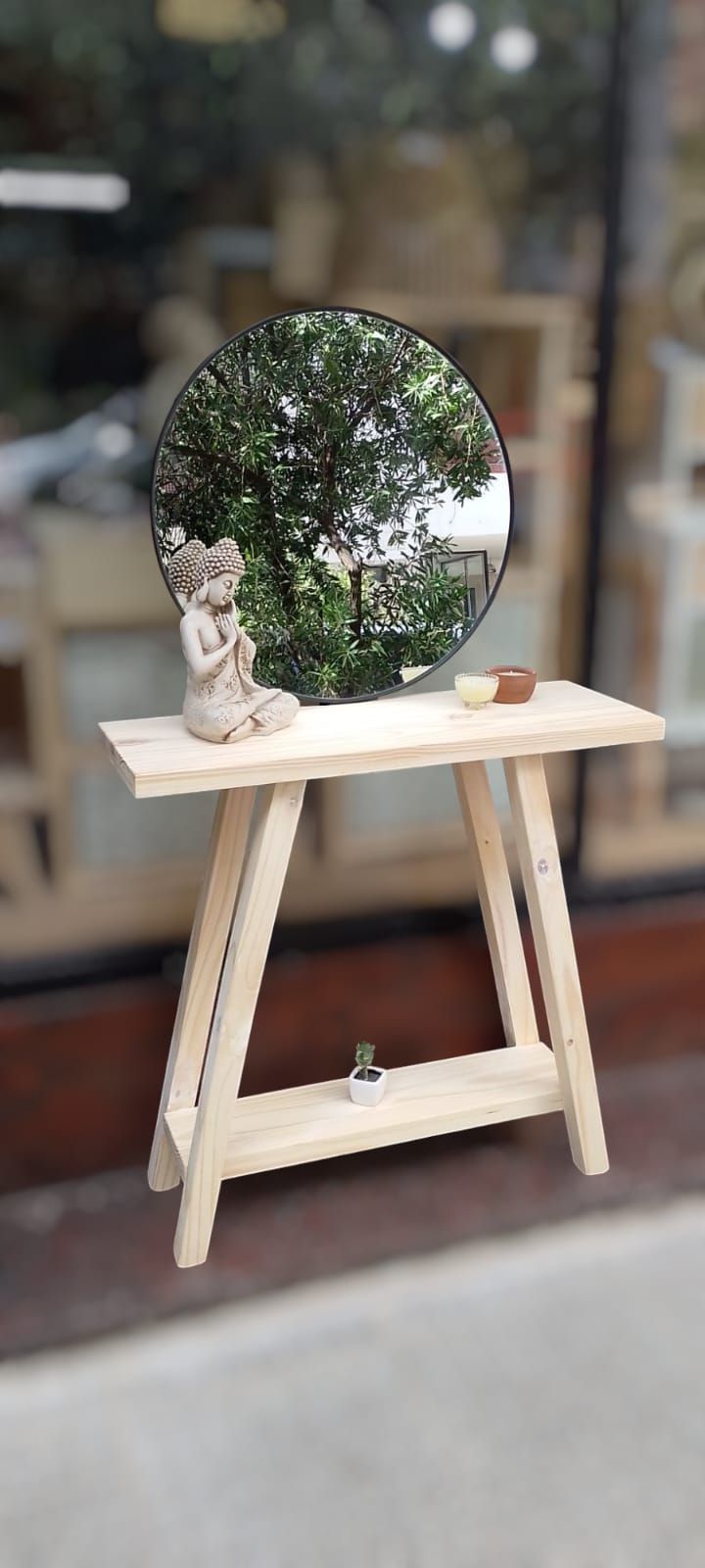 Consola de madera clara con espejo redondo, pequeño estante y decoración sobre un fondo rosa suave.