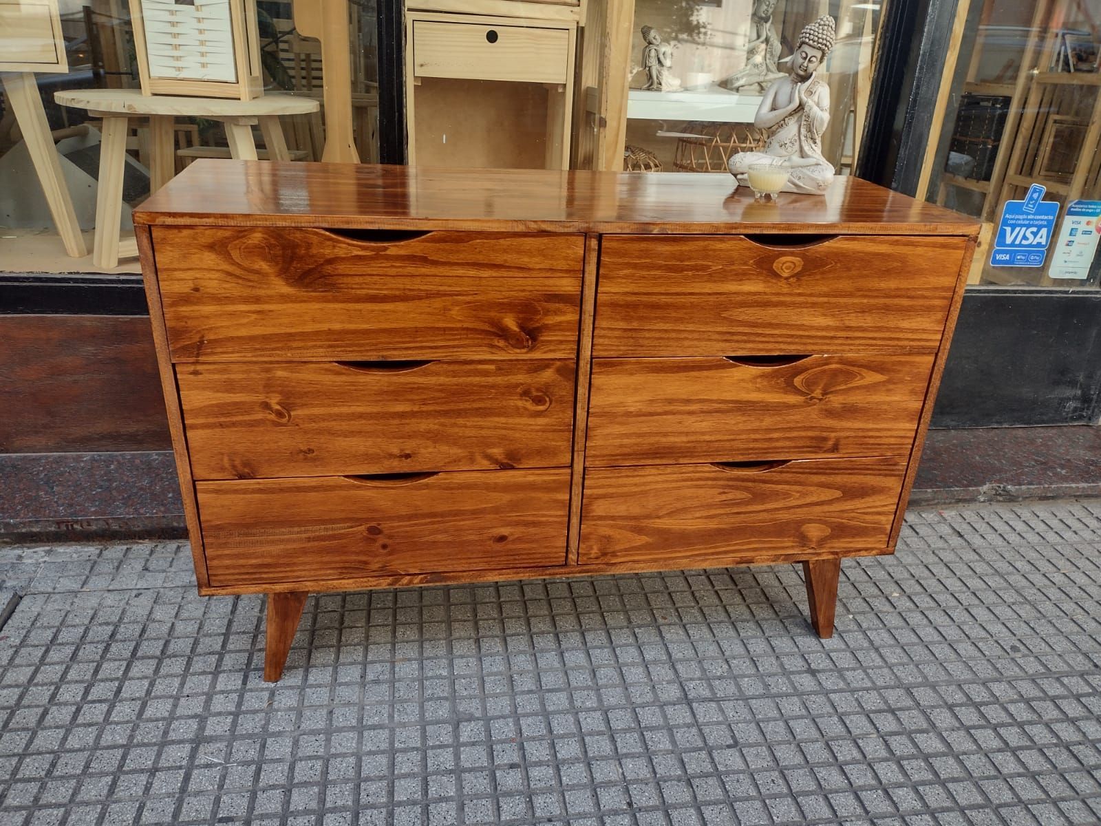 Una cómoda de madera con cajones blancos, colocada sobre una superficie gris al aire libre.