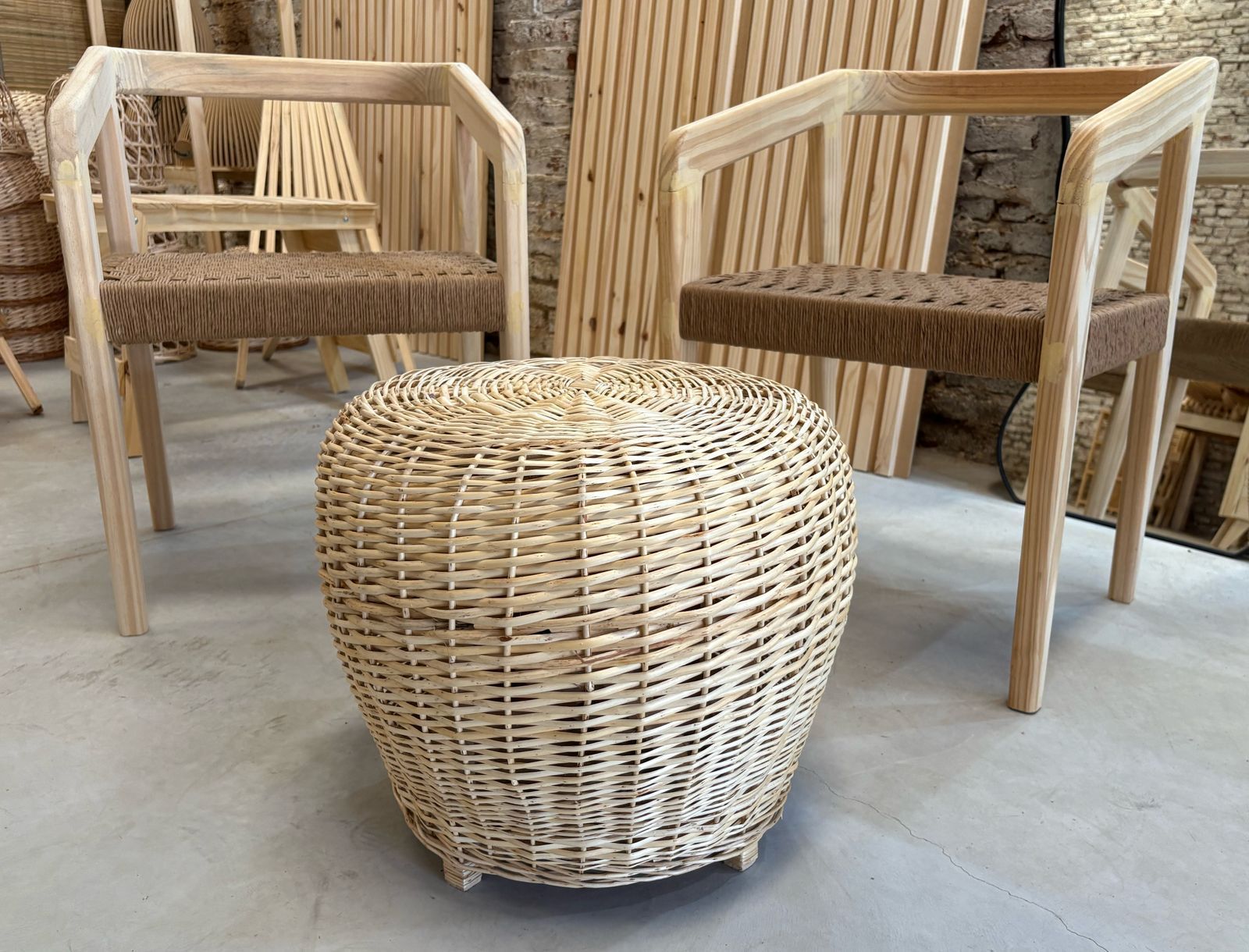 Otomana de mimbre sobre suelo claro. Tejido beige con pequeñas patas de madera.