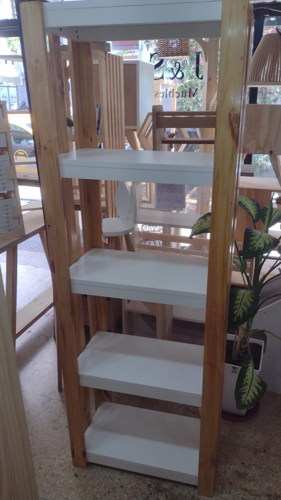 Estantería de escalera de madera con estantes blancos y marco de madera, parcialmente visible en un entorno exterior.