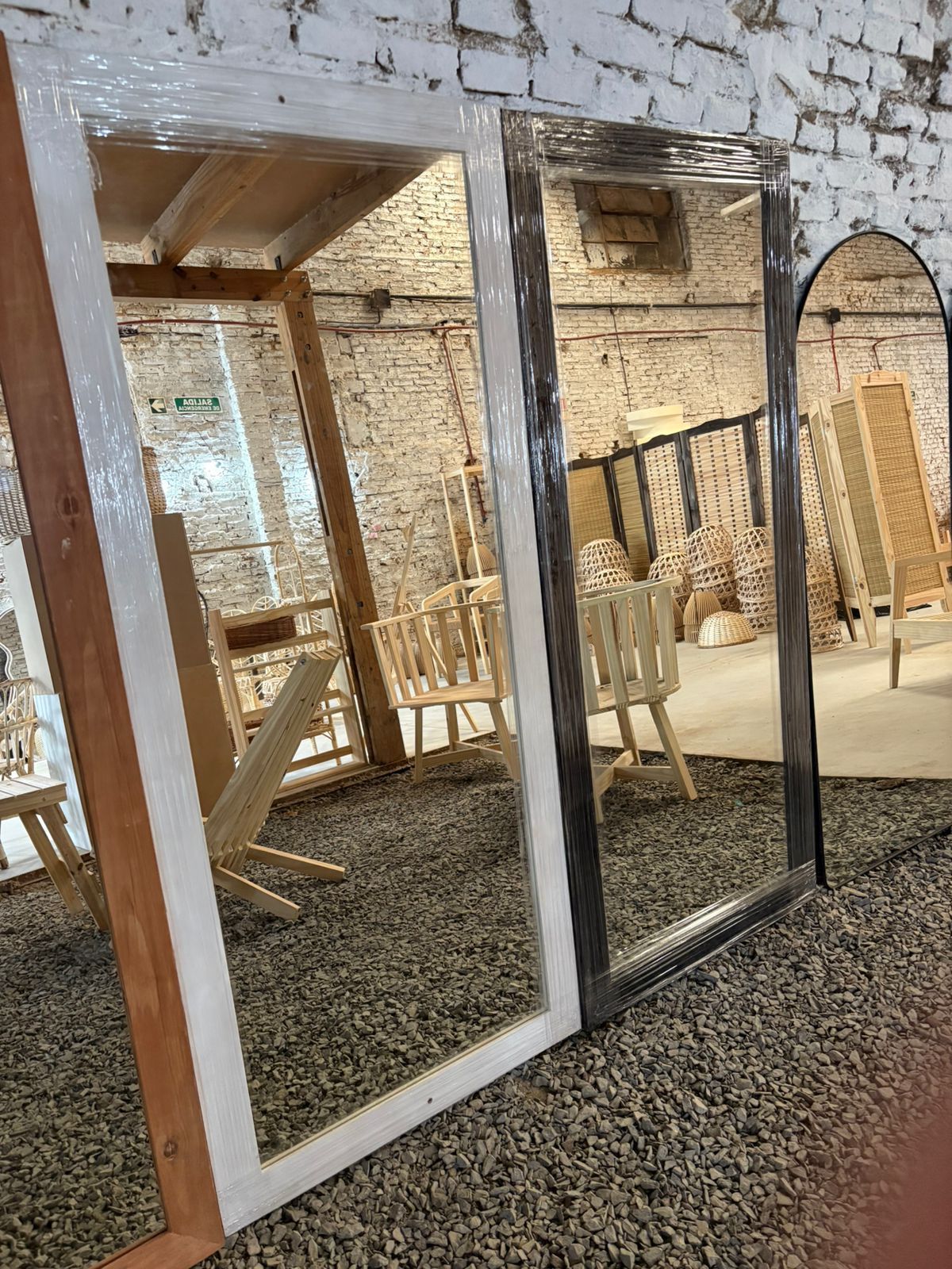 Dos espejos rectangulares con marcos de madera, uno claro y otro de color marrón rojizo, apoyados contra una pared de ladrillos.