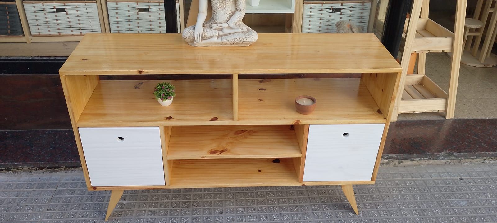 Mueble de madera con dos puertas blancas, estantes, pequeña planta y cuenco.