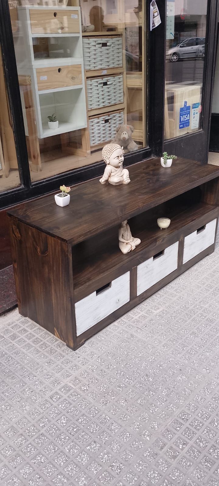 Un armario de madera con tres cajones blancos y estantes abiertos, decorado con estatuas y plantas.