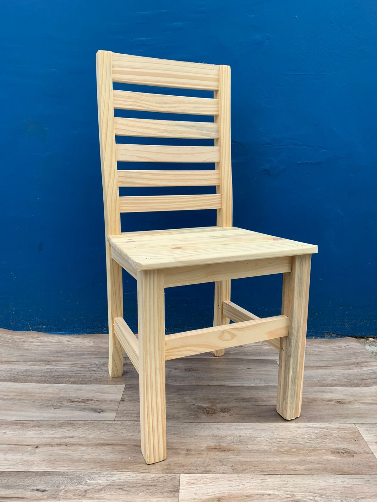 Silla de madera con respaldo de listones contra una pared azul.