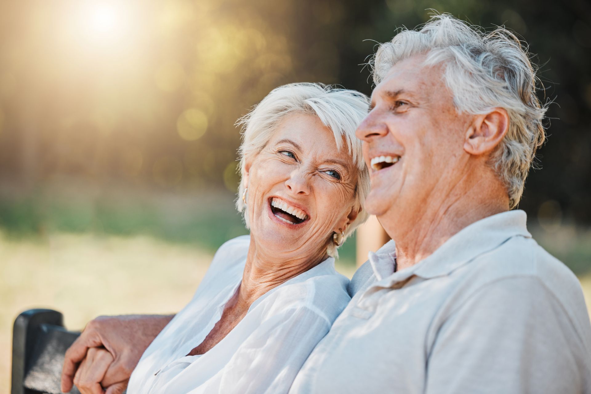 An elderly couple is sitting on a bench and smiling.
