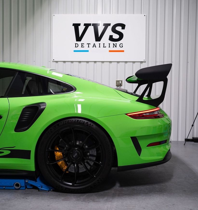 A green sports car is parked in front of a sign that says vvs detailing