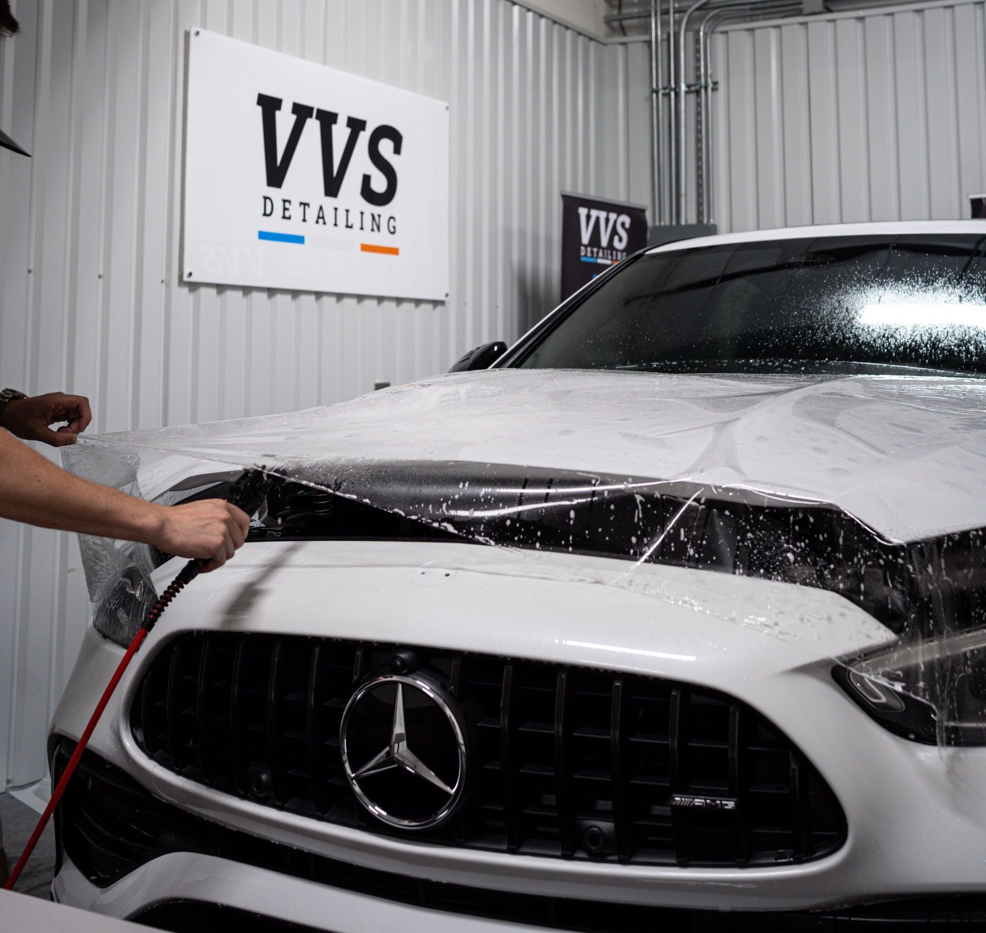 A person is applying a protective film to the front of a white mercedes benz.