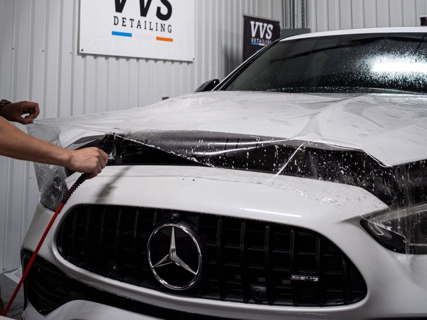 A person wearing black gloves is cleaning a car with a towel.