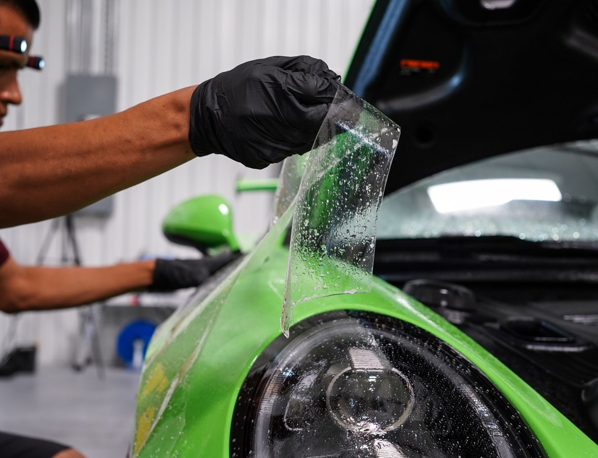 A man is applying a protective film to the side mirror of a car.