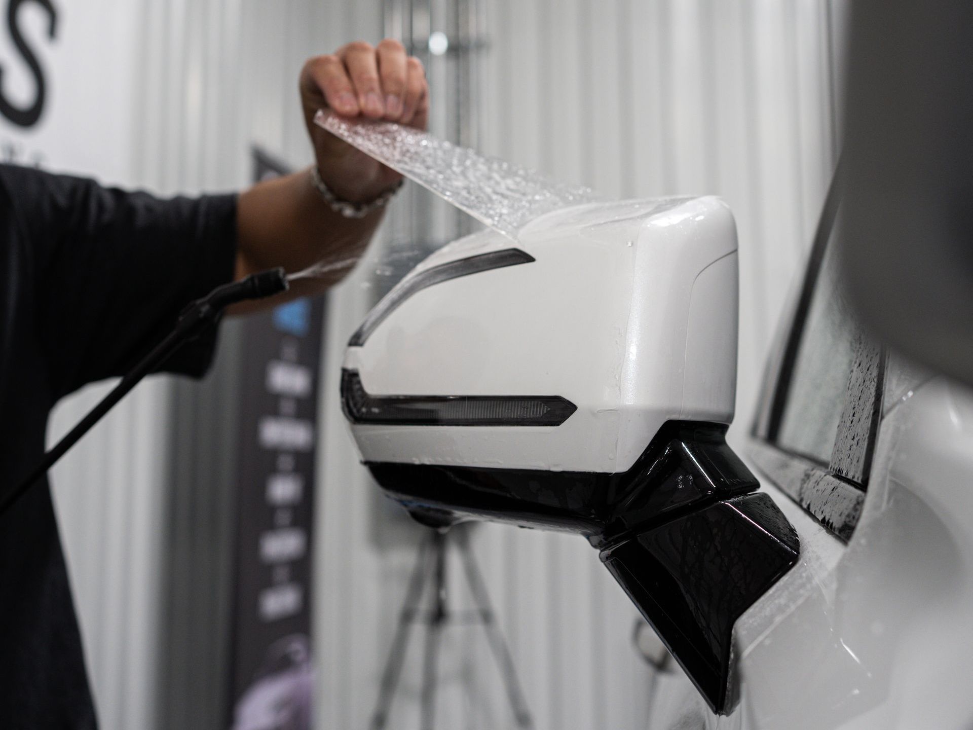 A person is wrapping a side view mirror on a white car.