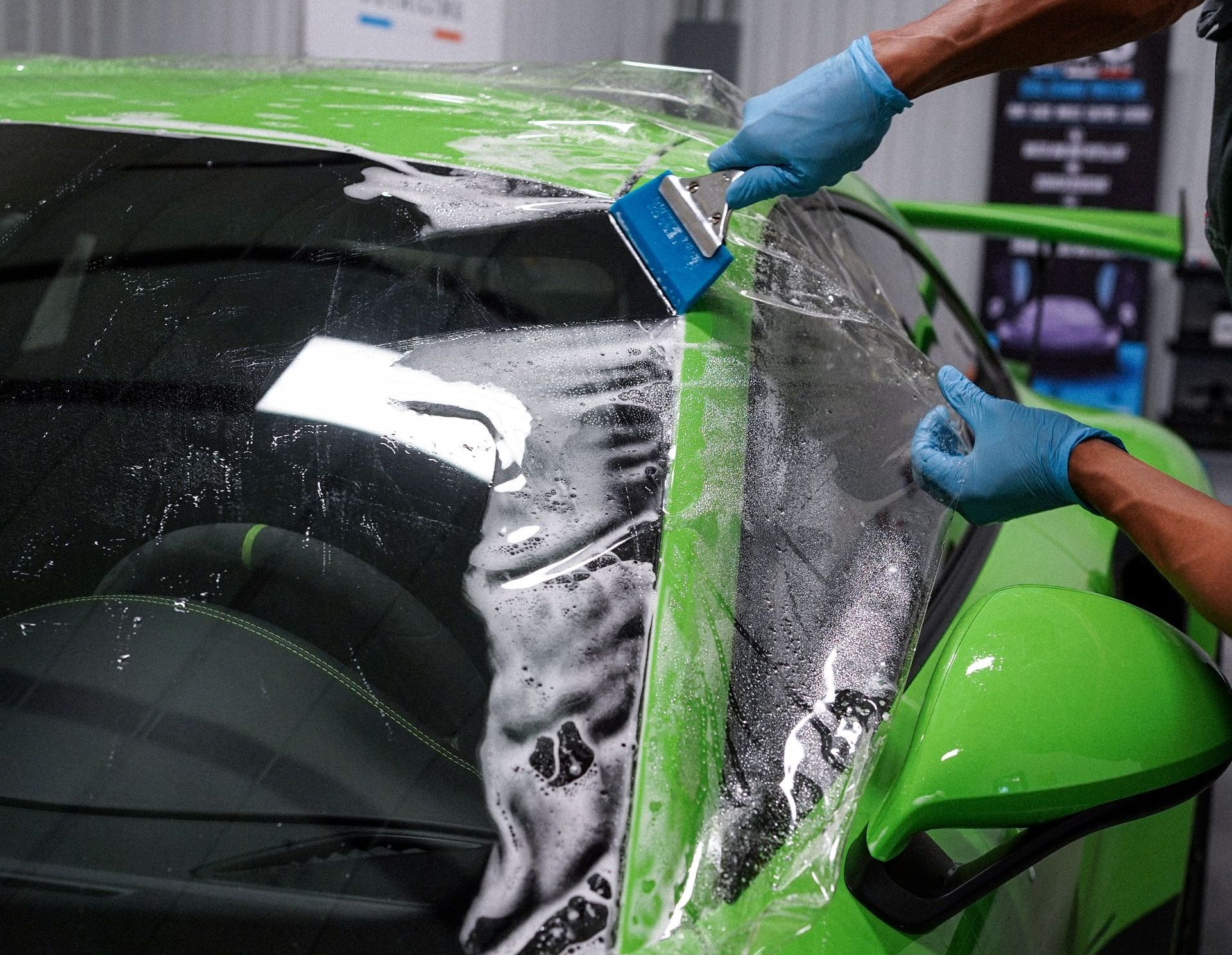 A man is sitting in a red car using a hair dryer to remove a sticker from the windshield.