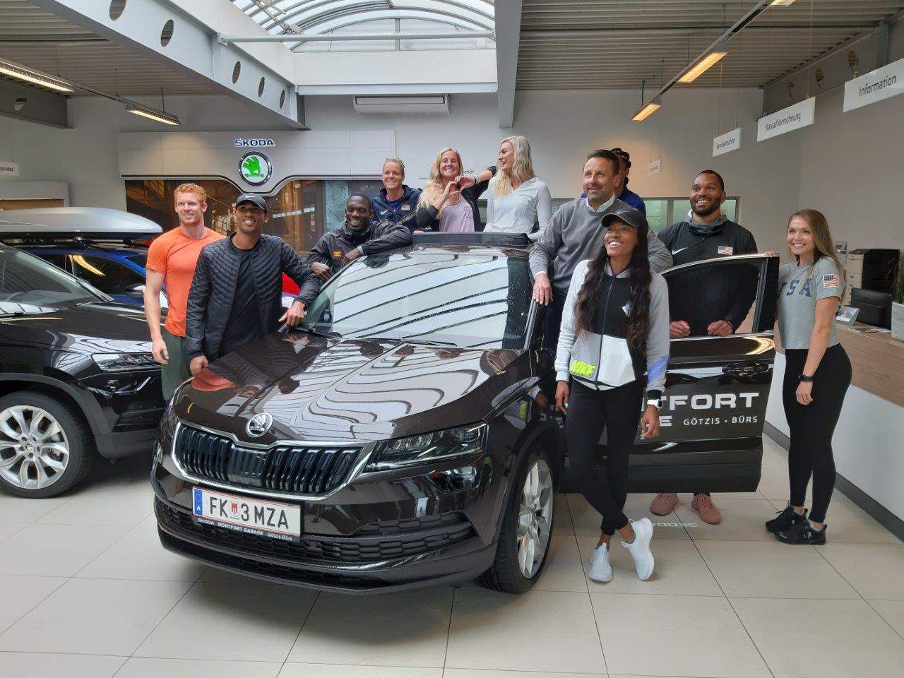 Gruppe von Mitarbeitenden steht vor einem Auto im Verkaufsraum, einige tragen Arbeitskleidung