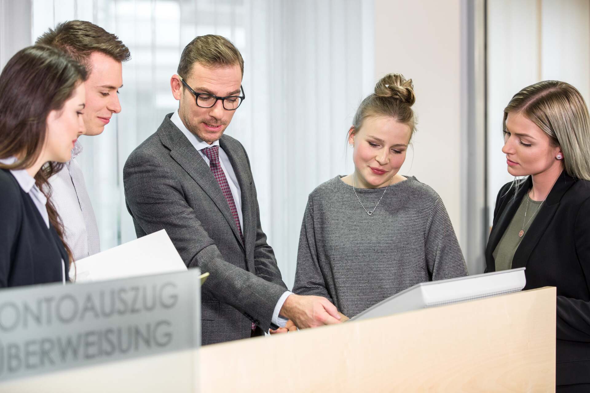 Fünf Mitarbeiter von der Raiffeisen in Businesskleidung besprechen gemeinsam ein großes Dokument