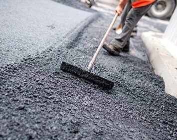 Worker Leveling Fresh Asphalt On A Road Construction Site — Asphalt Repairs in Arnold, MO