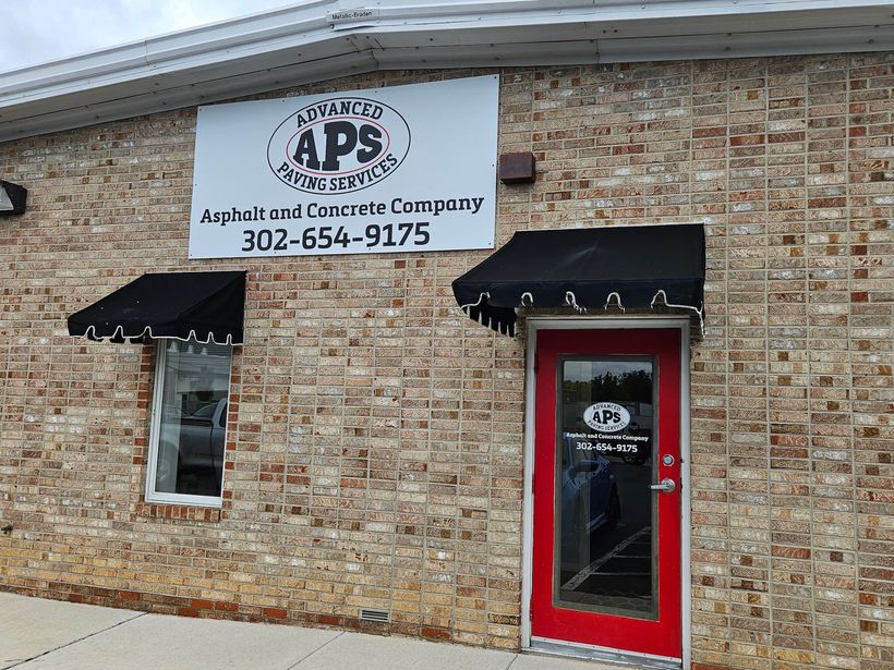 Brick building with black awnings over a window and red door. Signage: APS Augusta Paving and Concrete Company.