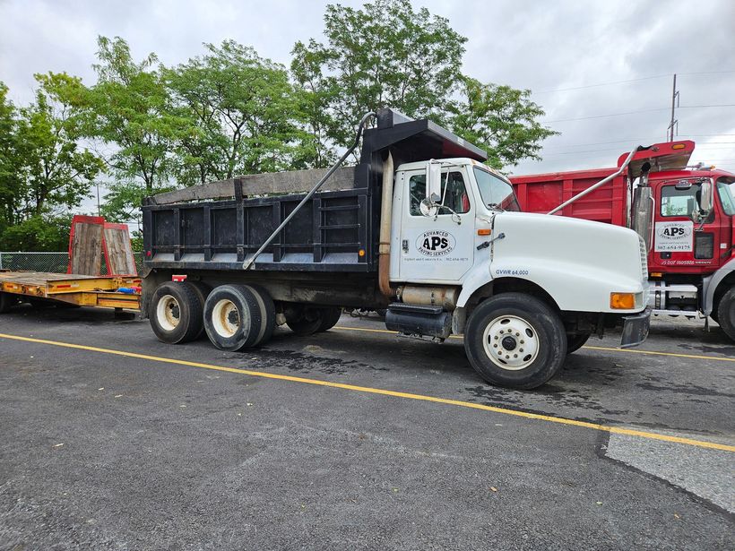 White dump truck parked on asphalt with a red truck nearby.