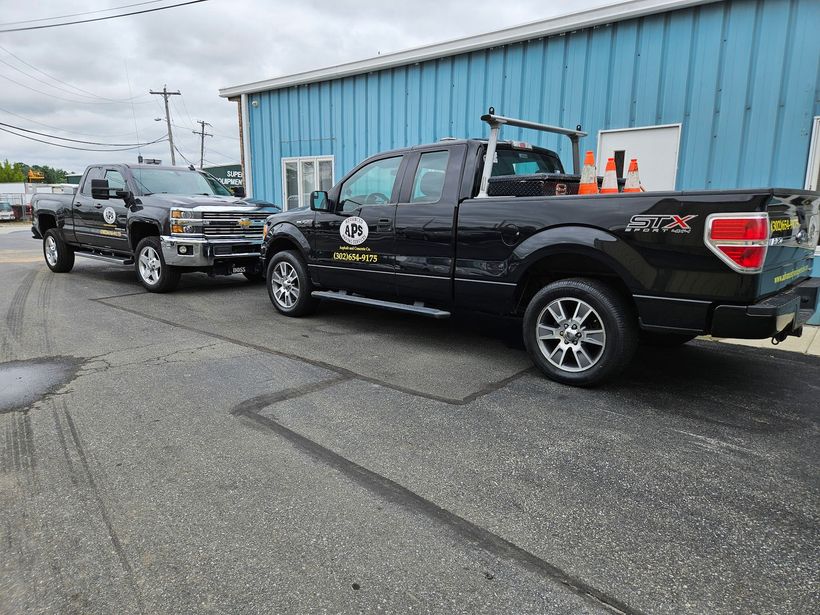 Two black pickup trucks parked on a gray asphalt road in front of a blue building.