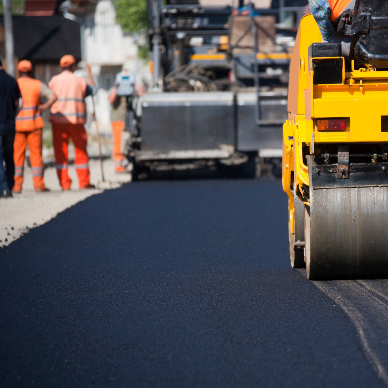 Yellow road roller compacting fresh asphalt on a road, workers in orange vests observe.