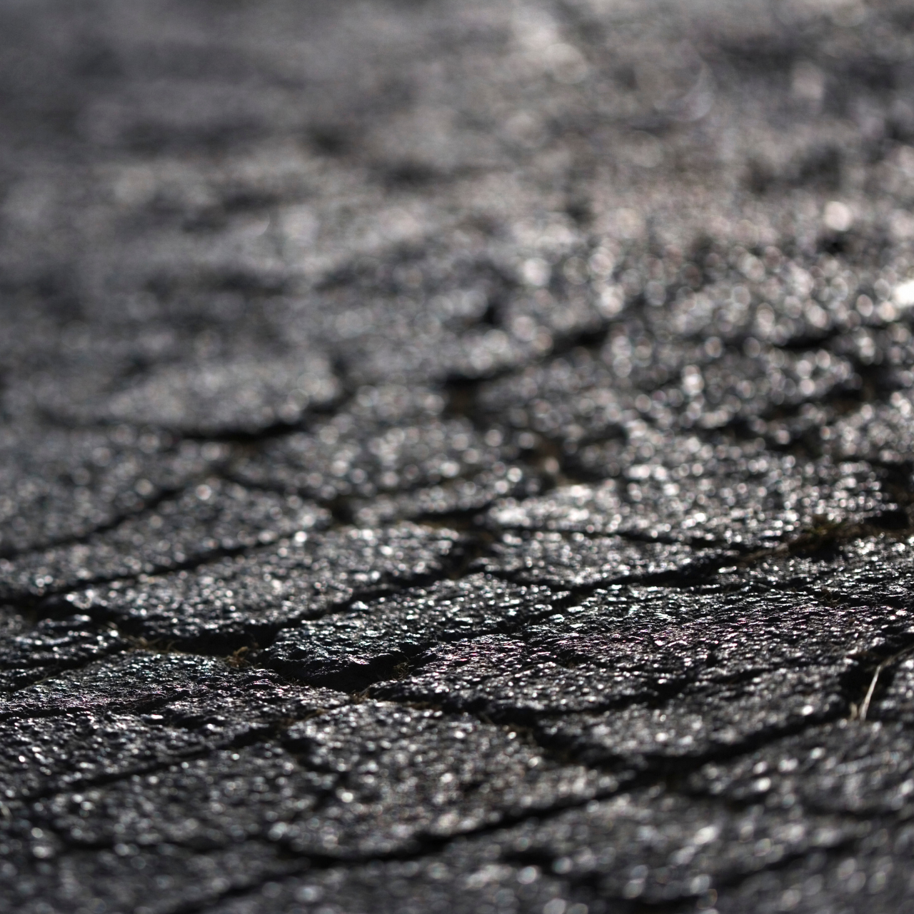 Close-up of dark, textured asphalt pavement, showing cracks and reflective surfaces.