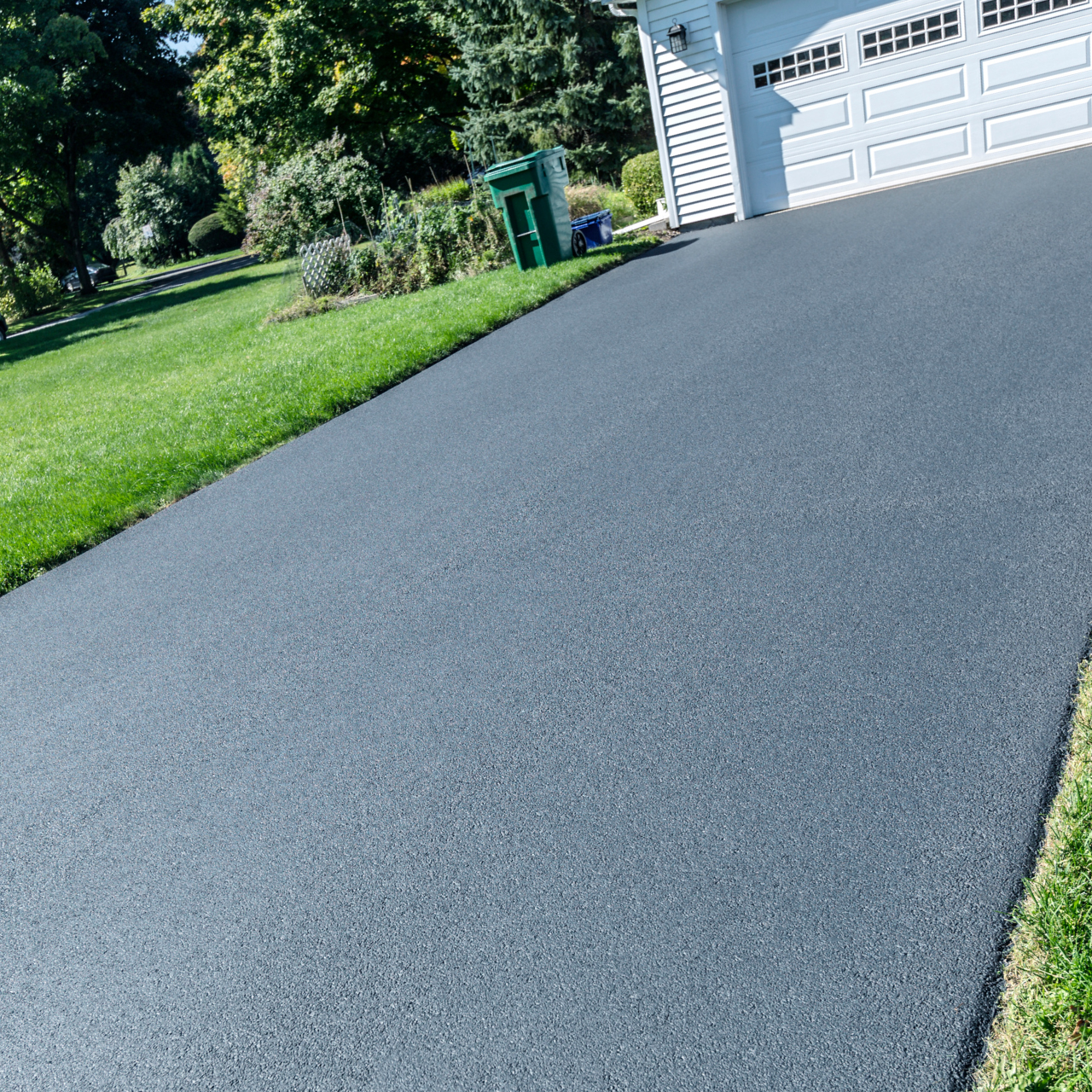 A freshly paved asphalt driveway next to a green lawn, leading to a white garage.