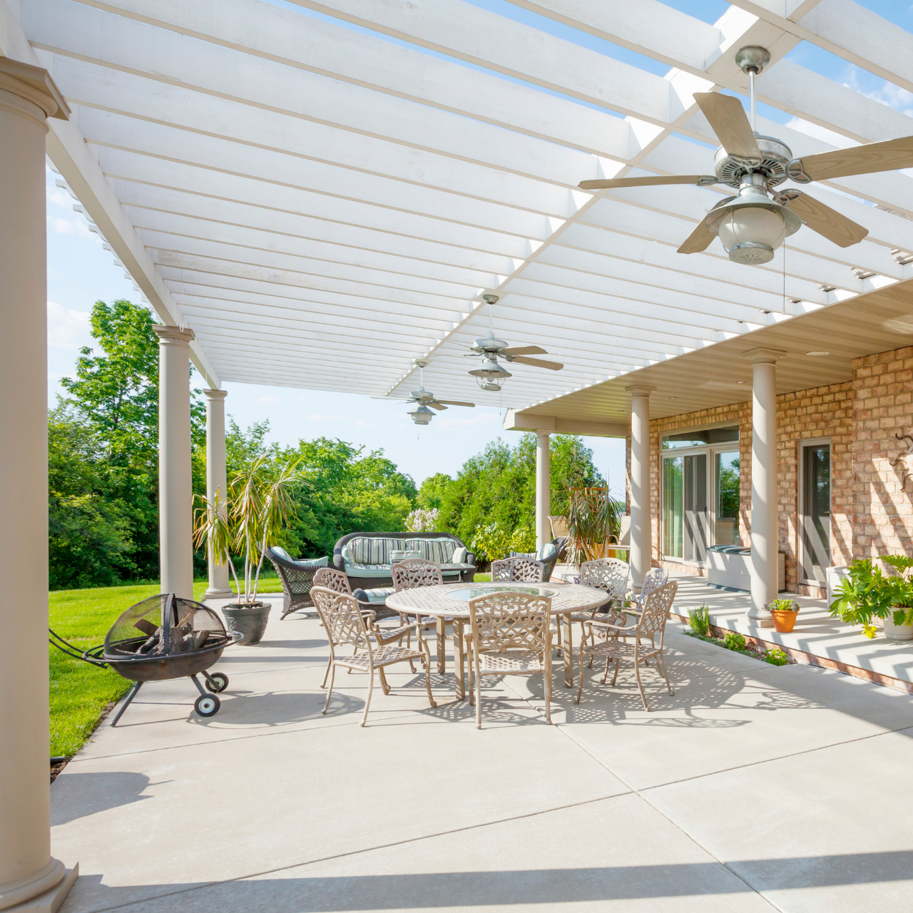 Patio with pergola, outdoor dining table, chairs, grill, and ceiling fans; sunny day.